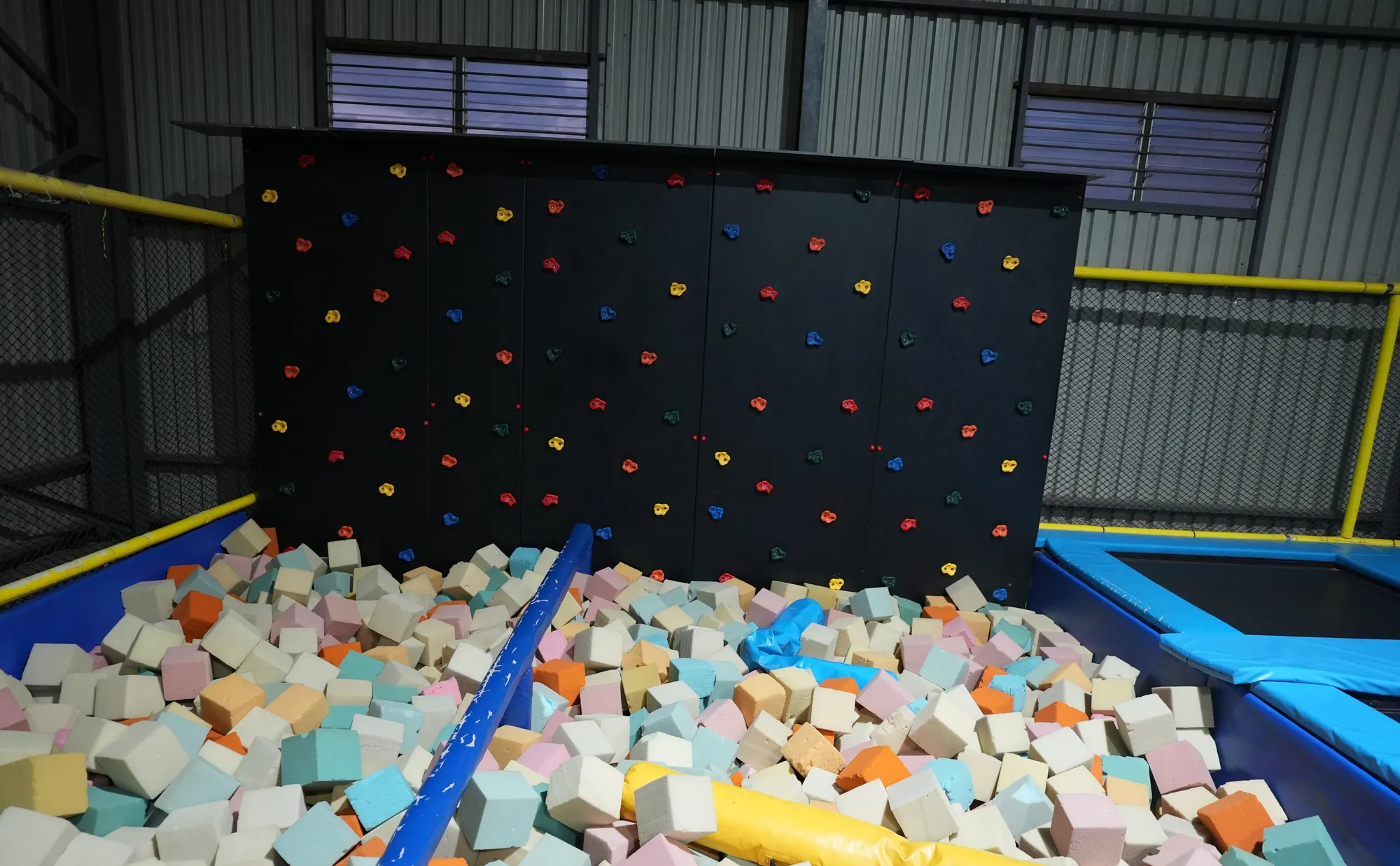 Black climbing wall with coloured holds above a foam pit at Jump Trampoline Park, Harare