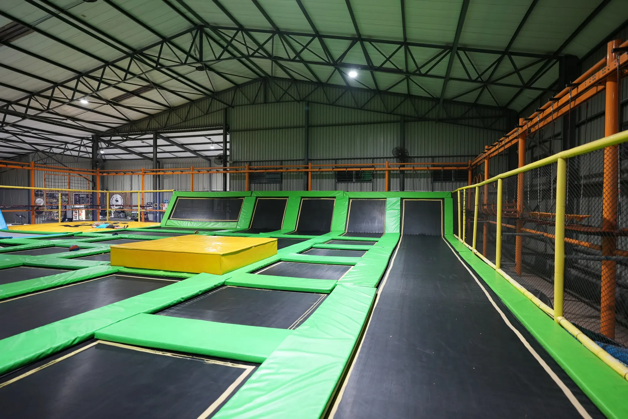 Green trampoline court with a yellow platform and a long black lane at Jump Trampoline Park, Harare