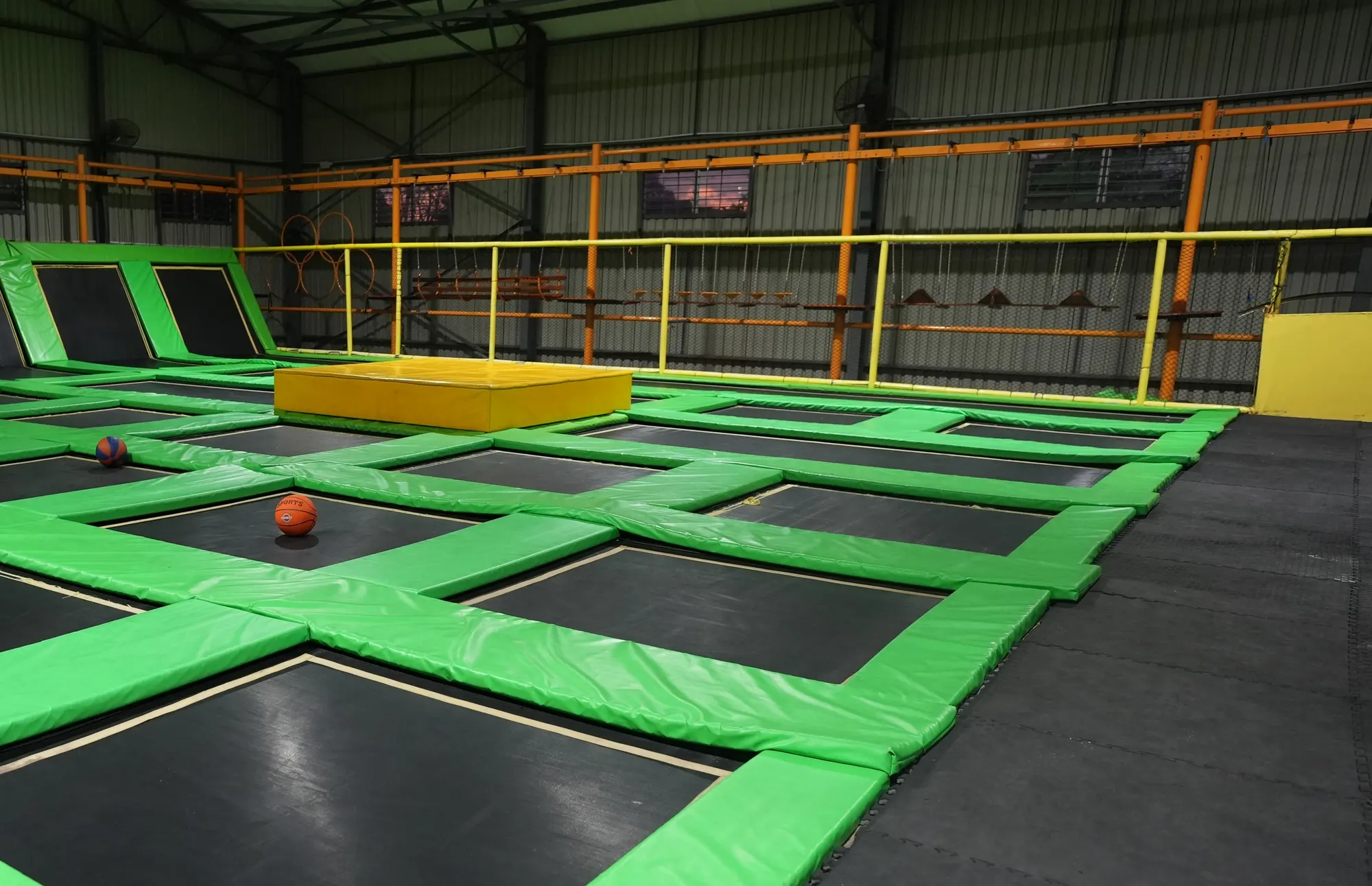 Green trampolines and a yellow platform in the open hall at Jump Trampoline Park, Harare
